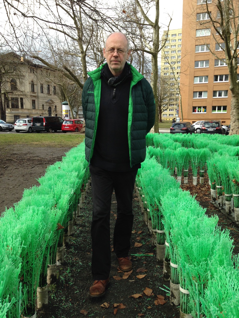 Auf dem Bild ist ein Mann zu sehen. Es handelt sich um den Komponisten Christoph Ogiermann. Er steht im Freien und trägt Winterkleidung. Im Hintergrund ist eine Stadtlandschaft zu sehen.